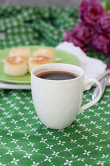 Black coffee in a white sophisticated cup, delicious dietary cheesecakes from home-made farmer cheese for breakfast, a bouquet of purple tulips on a green tablecloth.