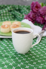 Black coffee in a white sophisticated cup, delicious dietary cheesecakes from home-made farmer cheese for breakfast, a bouquet of purple tulips on a green tablecloth.