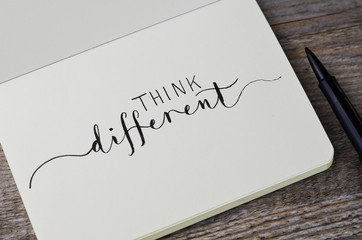 THINK DIFFERENT hand lettering in notebook with pen on wooden background