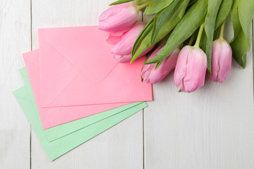 A bouquet of beautiful pink tulips flowers and color envelopes on a white wooden table. Spring. holidays. top view