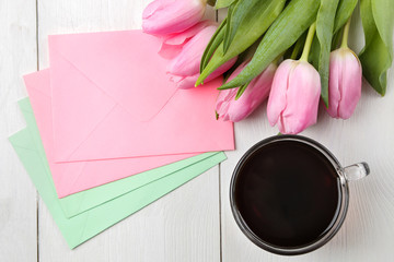 Fototapeta na wymiar A bouquet of beautiful pink tulips flowers and color envelopes and a cup of coffee on a white wooden table. Spring. holidays. top view