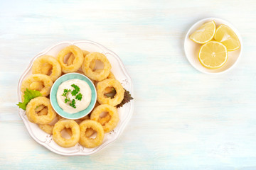 A photo of squid rings with mayo and lemon wedges, shot from the top, forming a frame for copy space