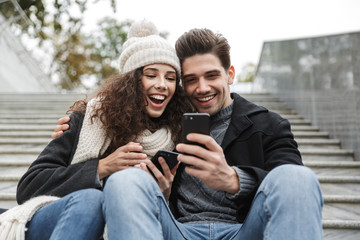 Happy young loving couple outdoors using mobile phone.