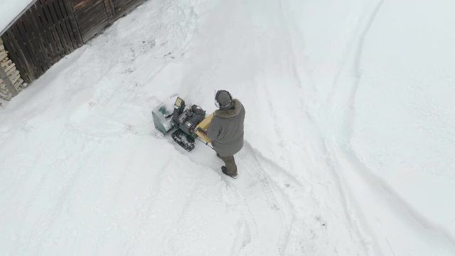 Aerial view of the man in coat pushing the snow plower