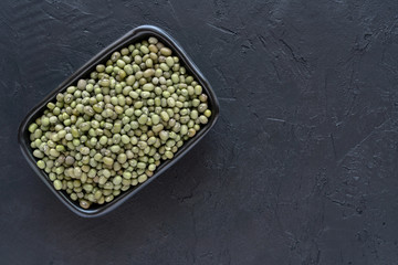 Dry green mung beans in a black  bowl on stone background