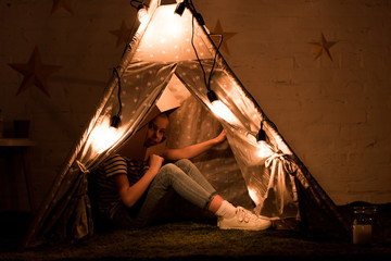 Preteen kid sitting in cozy wigwam with bulbs in dark room © LIGHTFIELD STUDIOS