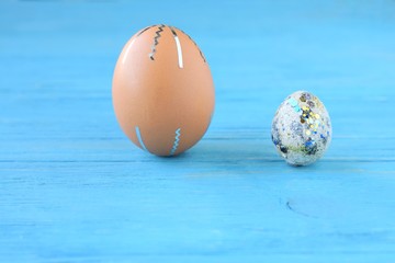 Brown chicken egg and quail spotted eggs with holiday Easter homemade decor on blue textured wood background with selective focus. Beautiful creative easter egg decor with blue shiny spots and stripes