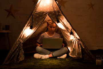 Concentrated kid using laptop in wigwam with luminous bulbs © LIGHTFIELD STUDIOS