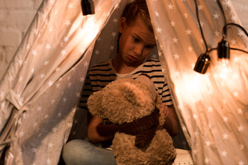 Disappointed kid looking at teddy bear while sitting in wigwam at home © LIGHTFIELD STUDIOS