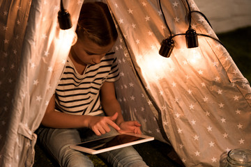 Kid in striped t-shirt sitting in wigwam and using digital tablet with blank screen © LIGHTFIELD STUDIOS