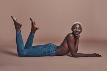 Smiling beauty. Attractive young African woman looking away and smiling while lying against brown...