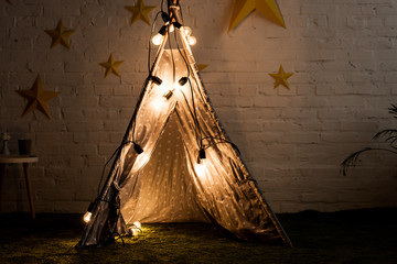 Cozy wigwam with luminous bulbs standing in dak room © LIGHTFIELD STUDIOS