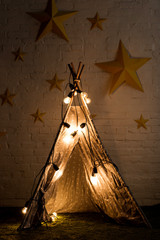 Cozy wigwam with luminous bulbs standing in dark room © LIGHTFIELD STUDIOS