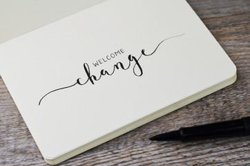 WELCOME CHANGE hand lettering in notebook with pen on wooden background - obrazy, fototapety, plakaty