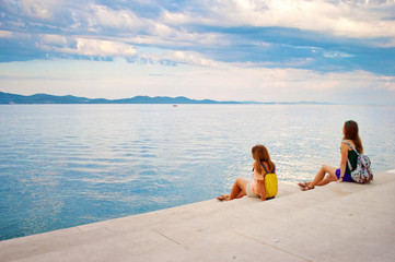 Two young girls with backpacks sitting on the stone stairs