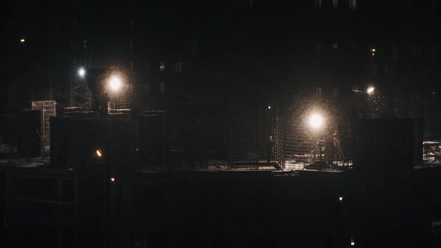 Construction site residential housing estate building, constructors working at winter night in bad weather conditions snowing