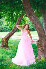 Obraz na płótnie Canvas Beautiful woman in pink dress posing in green summer park