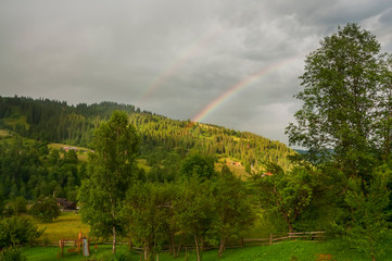 View of a high-mountainous small village in the forest. Rainbow over the mountains on a summer evening. The Carpathians Ukraine. The most high-rise village of Ukraine.