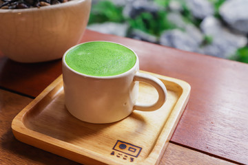 Close up Matcha green tea with seramic cup on wooden plate in japanese style garden background.