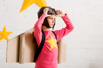Confident child with cardboard wings touching goggles