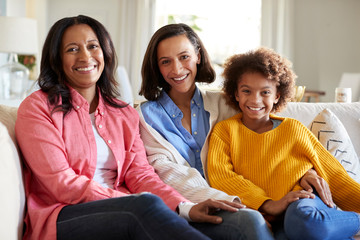 Three generation family female family group sitting on a sofa in the living room smiling to camera,...