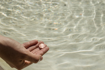 Mano tirando moneda al agua para pedir un deseo