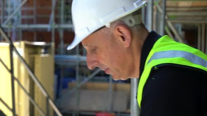Male builder foreman, worker or architect working on construction building site standing on scaffolding writing on clipboard 