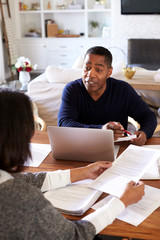Millennial man with laptop computer giving financial advice to a woman sitting at the table holding...