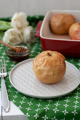 Baked apples in red, honey, a bunch of white tulips lie on a green tablecloth.