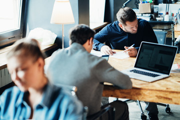 People work in the office. Wooden table with laptop and paperwork. Two men and woman employees