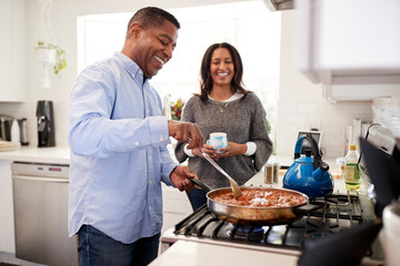 Millennial Hispanic man standing in the kitchen cooking with his partner standing beside him,...