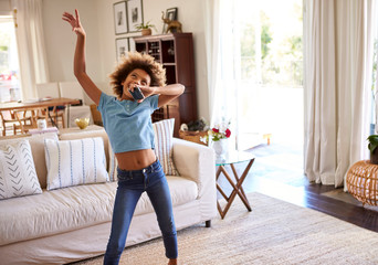 Pre-teen girl dancing and singing along to music in the living room at home using her phone as a...