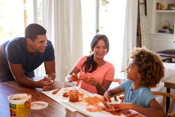 Millennial dad leaning on table watching his daughter and her girlfriend playing with modelling clay in the dining room