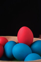 Colored easter eggs on black background. Red egg on top on blue eggs. Selective focus