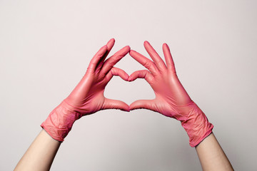 Closeup of a hand in latex rubber medical pink gloves folded into a heart sign. Isolated on white background. Concept love couple couple valentine