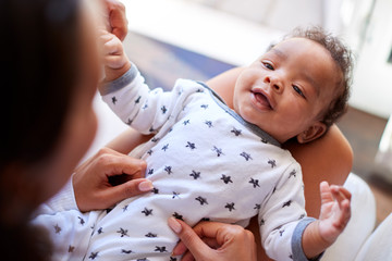 Happy three month old baby boy lying on his back on his motherâ€™s knee looking up at her, over shoulder view, close up