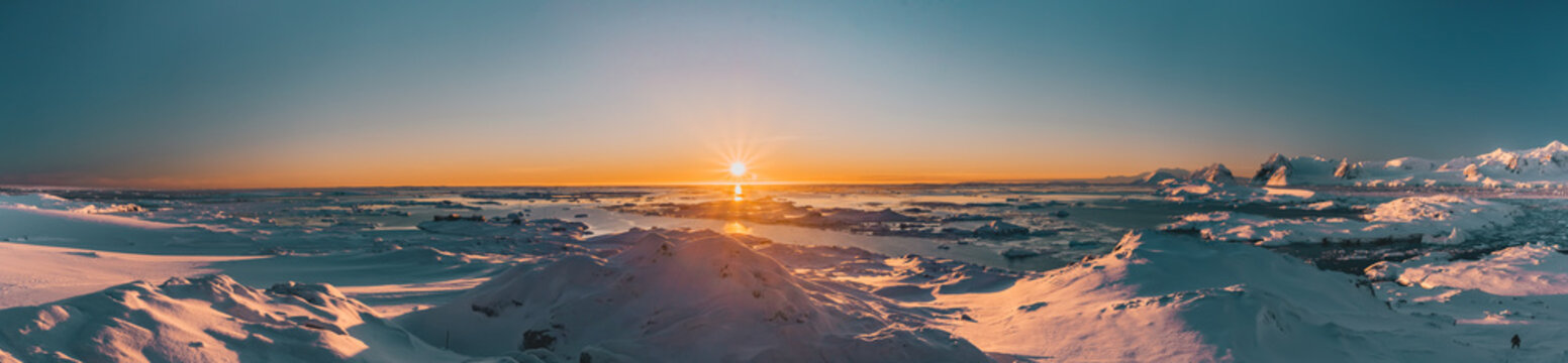 Bright colorful sunset panorama view in Antarctica. Orange sun lights over the snow covered polar surface. Picturesque winter landscape. The beauty of the wild untouched Antarctic nature.