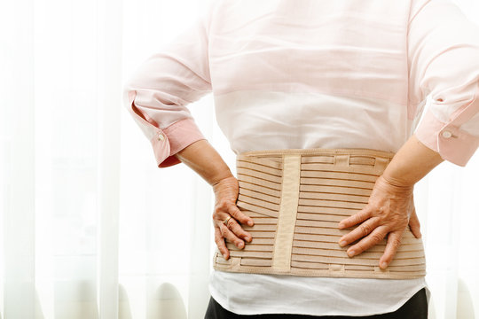 back pain, senior woman wearing back support belt on white background