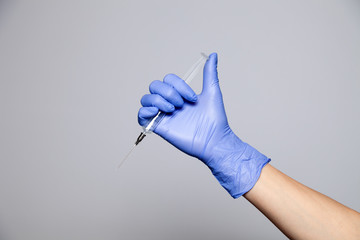 Closeup hand in rubber latex medicine purple glove holding transparent syringe with a sharp needle....