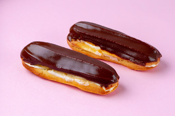 Traditional french dessert. Delicious eclairs with custard and chocolate icing on pink background. Pastry products for sweet tooth