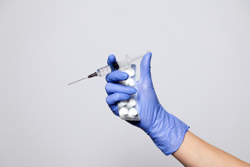Closeup doctor's hand in rubber latex purple glove hold transparent syringe and pills in blister....
