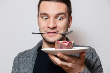 Closeup portrait young cute caucasian man smile, hold fork in his teeth and white round plate with...