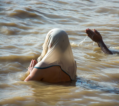 Mujer de espaldas ba&ntilde;&aacute;ndose y rezando en el r&iacute;o Ganges, con pa&ntilde;uelo blanco, en Varanasi, India