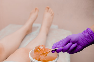 Wax bar with sugar paste depilation and beauty concept - sugar paste or wax honey for hair removing with bright  purple gloves hands of cosmetologist in spa salon. Top view several objects