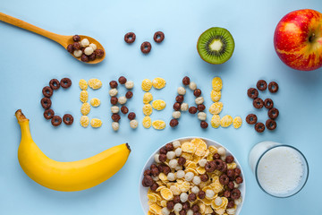 Bowl and spoon with dry chocolate balls, rings, corn flakes, glass of milk and fresh ripe fruits...
