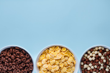 Cereals bowl with chocolate balls, rings and yellow corn flakes for dry breakfast on blue background. Copy space, top view