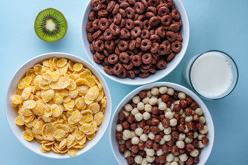 Cereals bowl of glazed, chocolate balls, rings, cornflakes, ripe kiwi and a glass of fresh milk for...