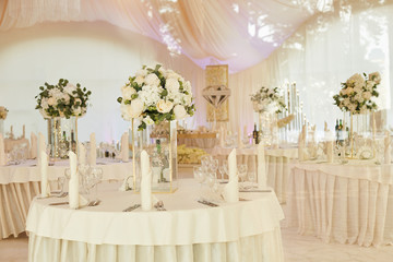 Banquet room with dining tables for guests during the wedding ceremony. The tent is decorated with white cloth.