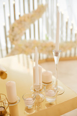 White tall candles in glass candlesticks on the table are colored gold in the banquet hall