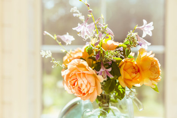 Valentine's Day, orange English rose flowers in a glass jar on the background of a large window of a wooden house, space for text, vintage style, retro interior with flowers.